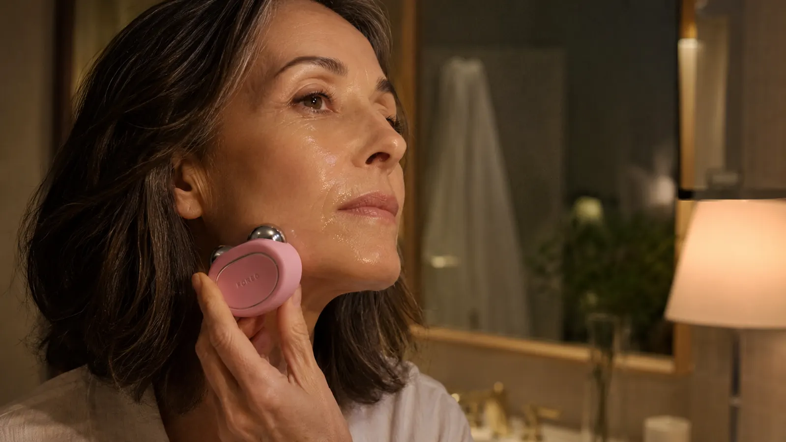 Hand holding the FOREO Bear microcurrent device against a jawline with conductive gel visible