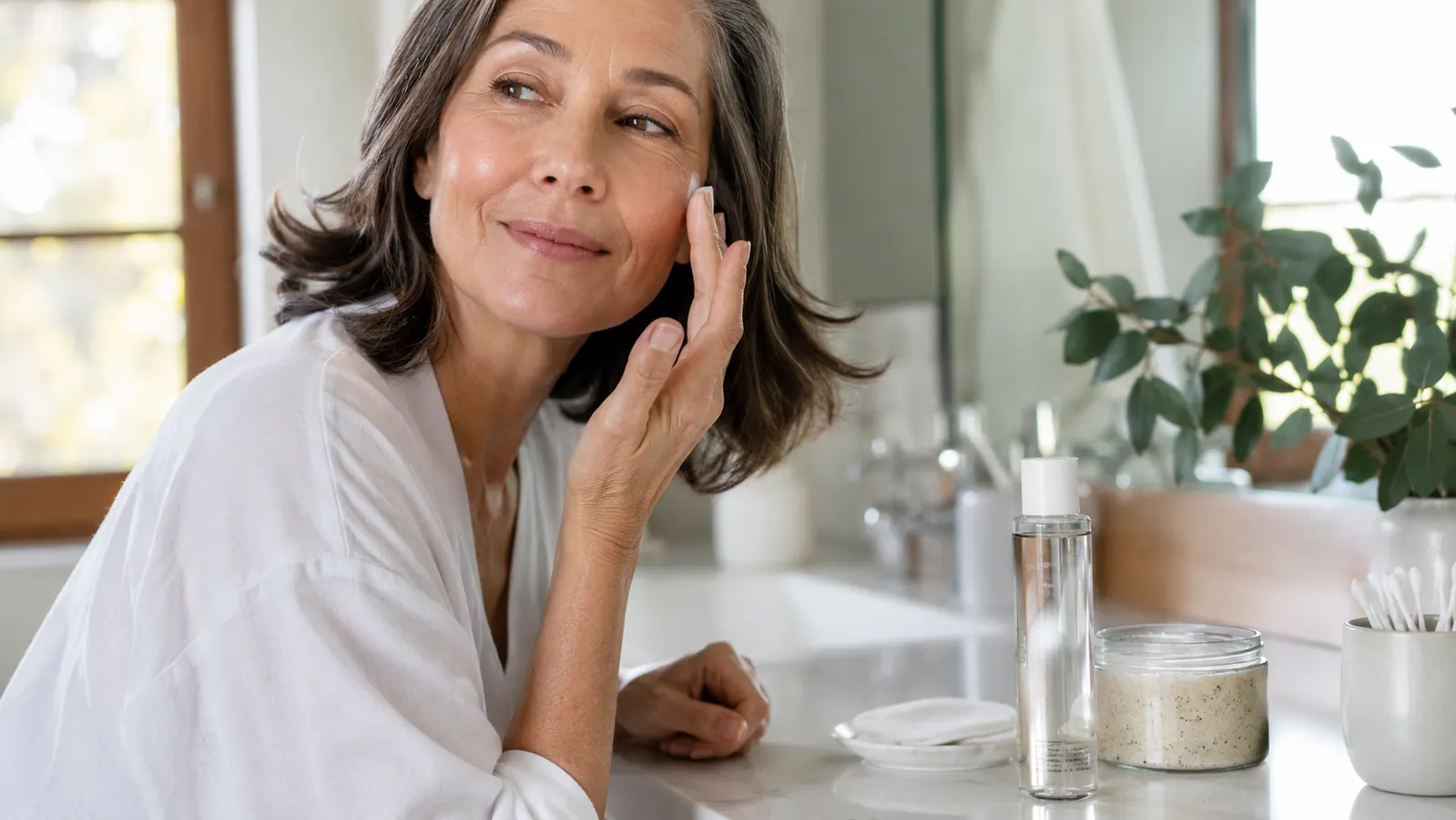 A bottle of Paula's Choice 2% BHA Liquid Exfoliant next to a jar of gritty apricot scrub on a bathroom counter