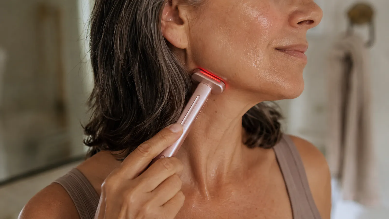 Close-up of a hand pressing the Solawave wand along the side of a neck with serum visible on the skin